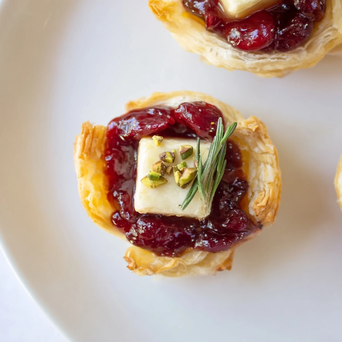 Golden puff pastry Mini Cranberry Brie Tart Wreath with melting cheese, vibrant cranberry topping, ready to eat.