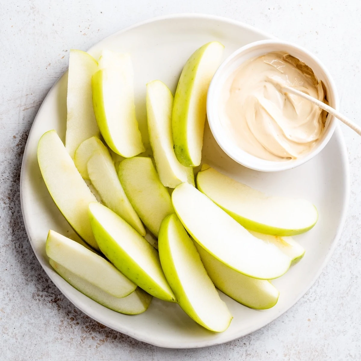 Crisp apple slices surrounding a small bowl of creamy peanut butter dip—a simple snack.