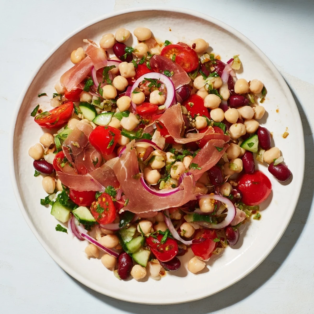 A close-up of Dense Bean Salad with Prosciutto, glistening with vinaigrette and fresh herbs.