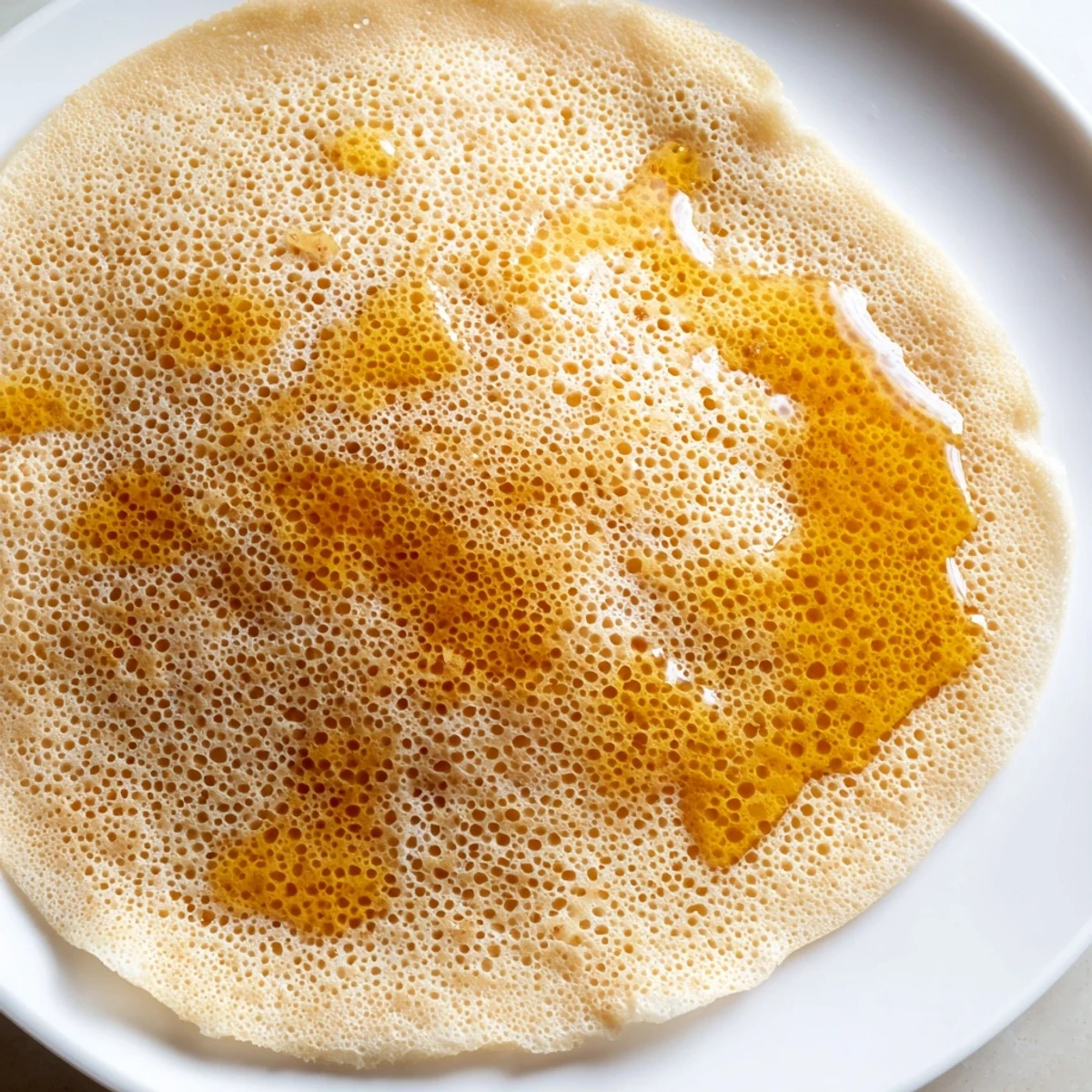 Fluffy Moroccan Baghrir crepes are bubbling, offering a delicious breakfast delight drizzled with honey.