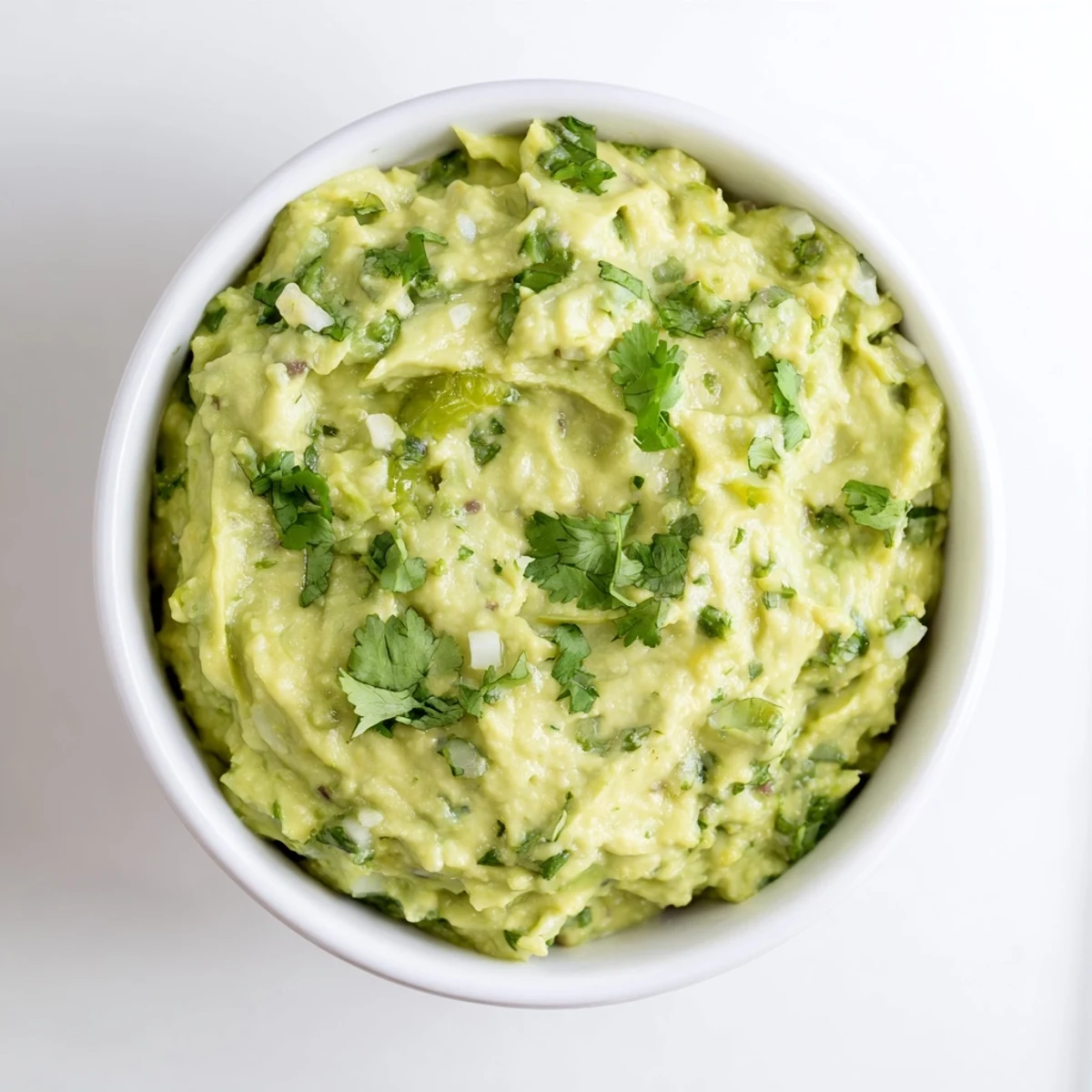 Freshly mashed avocado dip garnished with cilantro and lime slices, served in a rustic bowl with colorful vegetable crudités for dipping.