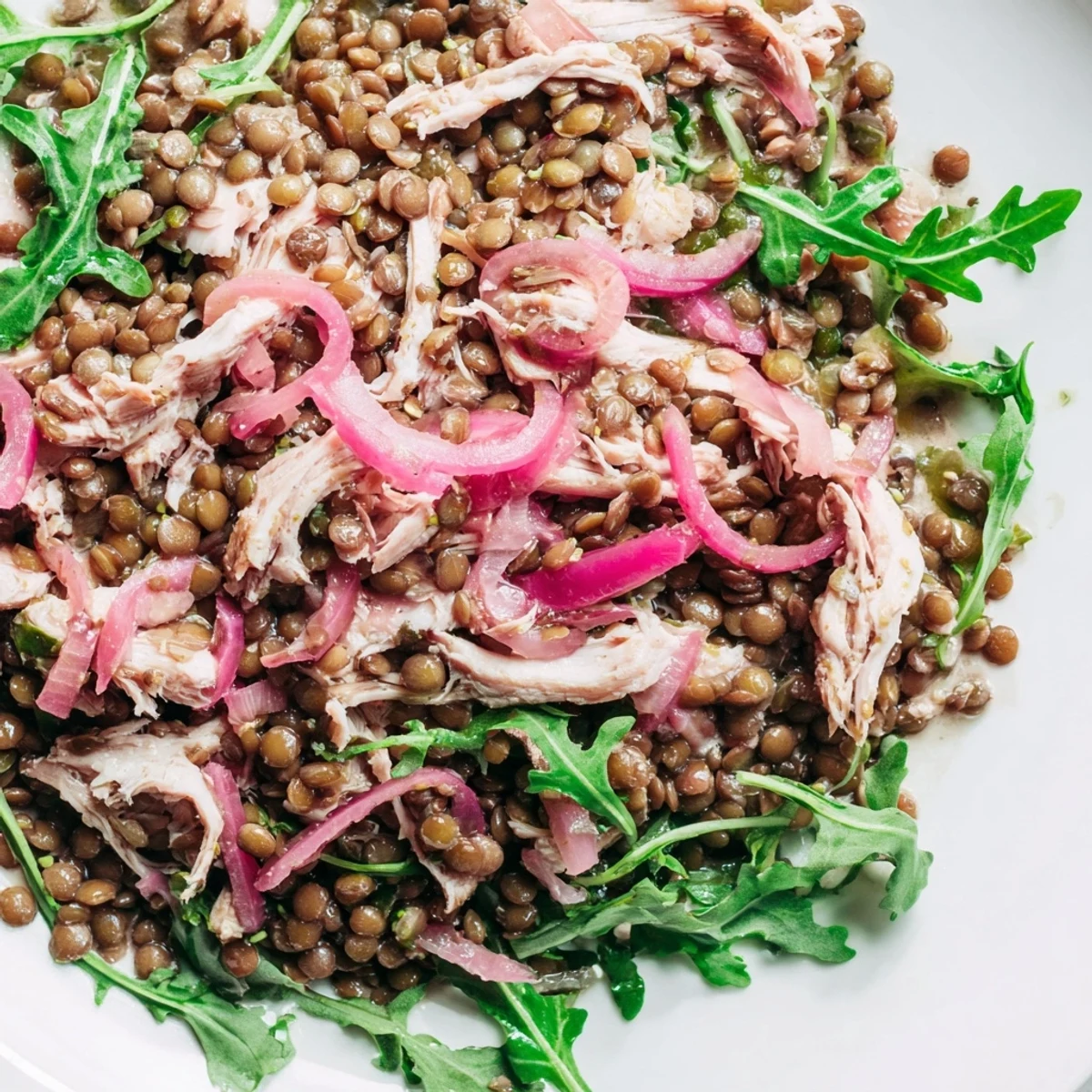 A close-up of Lentil & Chicken Spring Salad with tender lentils, juicy shredded chicken, and fresh arugula in a zesty mustard dressing.
