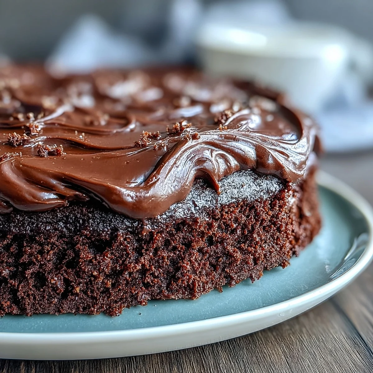 A close-up of Easy Chocolate Fudge Cake showing a moist crumb, glossy chocolate coating, and a dollop of fresh whipped cream.
