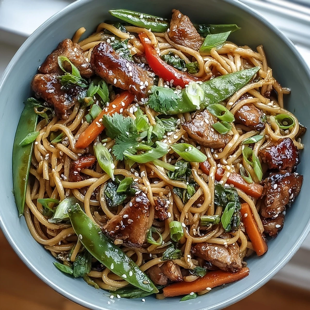 A close-up view of glossy noodles and sliced pork in a rich sauce, garnished with green onions for this Pork Noodle Stir-Fry.