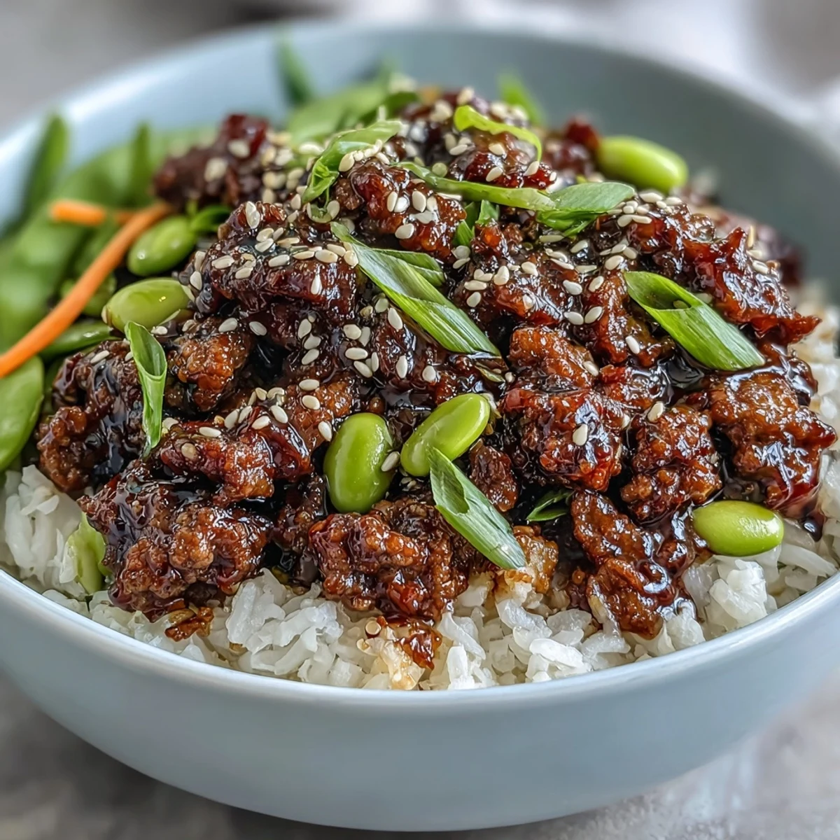 Savory Korean Ground Beef Bowl served with edamame, sliced cucumbers, and a drizzle of sesame oil.