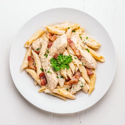 Creamy Chicken Bacon Penne twirled on a fork, showcasing smoky bacon bits and tender chicken in a garlic-Parmesan cream sauce.