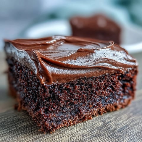 Easy Chocolate Fudge Cake layered with silky icing on a white plate, ready to slice and serve at a celebration.