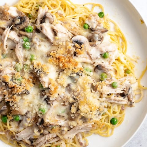 A bubbling casserole dish of Turkey Tetrazzini showcases pasta, turkey, and mushrooms in a rich sauce.
