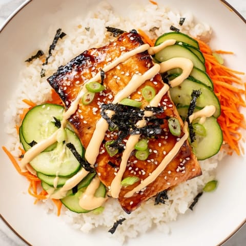 A close-up of a teriyaki salmon rice bowl, showcasing tender salmon over fluffy rice with toppings.