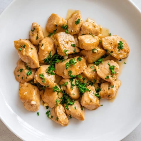 Golden-brown Creamy Garlic Chicken Bites simmer in a rich, creamy garlic sauce, garnished with fresh parsley and served alongside fluffy white rice.