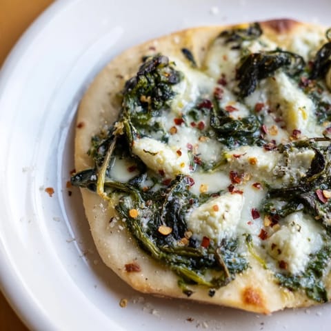 A close-up of creamy spinach ricotta pizza topped with sautéed spinach, garlic butter, and melted mozzarella on a golden crust.  