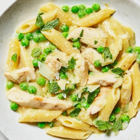 A close-up of Pea & Mint Chicken Pasta in a creamy Parmesan sauce, garnished with fresh mint.  