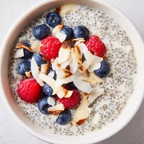 Poppy seed chia pudding in a white bowl, garnished with shredded coconut and fresh berries, perfect for a healthy breakfast.