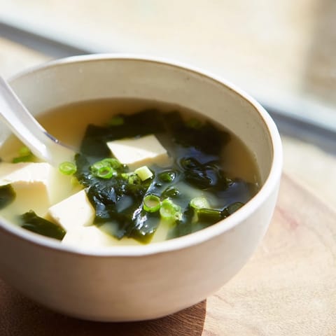 Serving of nourishing wakame soup garnished with fresh scallions, featuring tender tofu and rehydrated seaweed.  