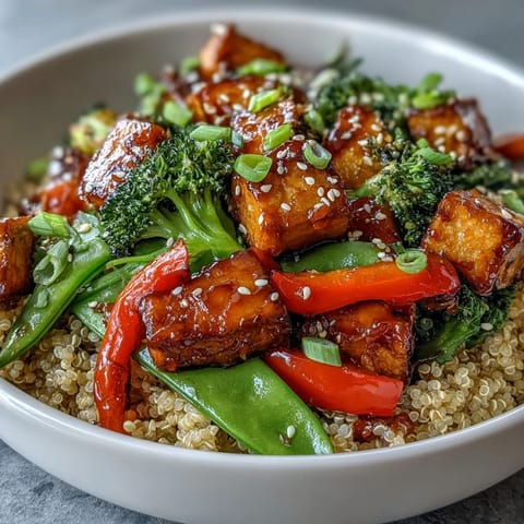 Golden crispy tofu cubes and vibrant stir-fried vegetables sit atop fluffy quinoa, drizzled with glossy teriyaki sauce in the Quinoa Vegetable Teriyaki Bowl.