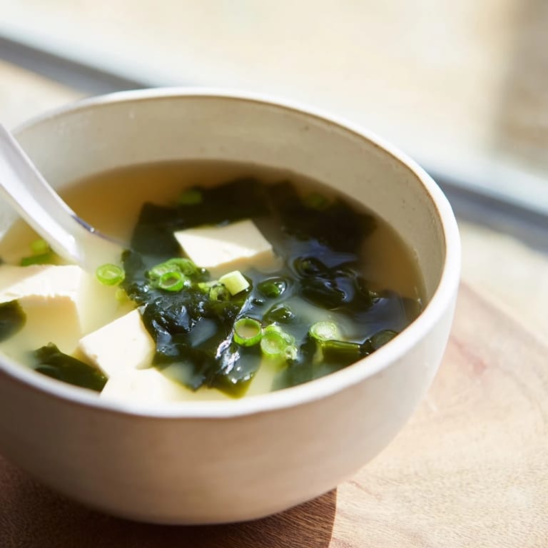 Serving of nourishing wakame soup garnished with fresh scallions, featuring tender tofu and rehydrated seaweed.  