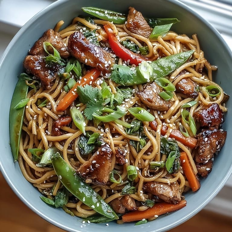 A close-up view of glossy noodles and sliced pork in a rich sauce, garnished with green onions for this Pork Noodle Stir-Fry.