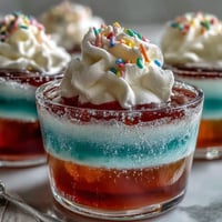 Vibrant rainbow Jello cups with fruity layers and whipped cream topping, perfect for kids' parties and celebrations.