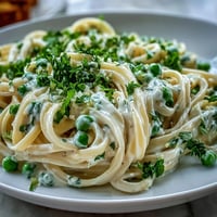Spring Pasta with Lemon Cream Sauce and Peas in a creamy skillet with fresh spinach and chives. Spring Pasta with Lemon Cream Sauce and Peas garnished with Parmesan and lemon zest on a white plate. Vibrant Spring Pasta with Lemon Cream Sauce and Peas served with a side of crisp white wine and fresh bread.